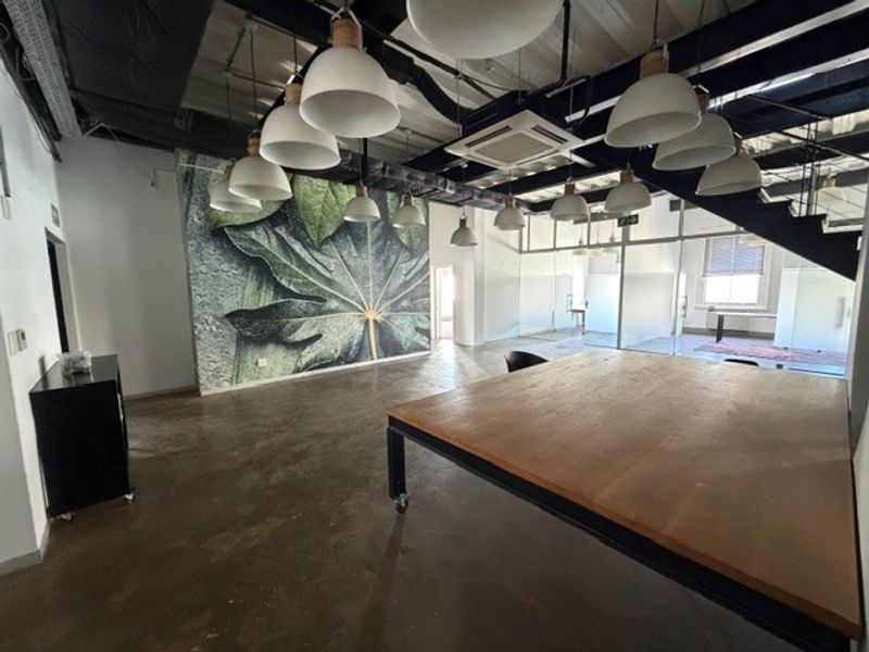 Modern open-plan office space featuring industrial-style exposed ceilings, polished concrete floors, contemporary pendant lighting, and glass-partitioned meeting areas.