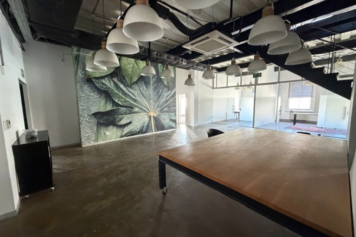 Modern open-plan office space featuring industrial-style exposed ceilings, polished concrete floors, contemporary pendant lighting, and glass-partitioned meeting areas.