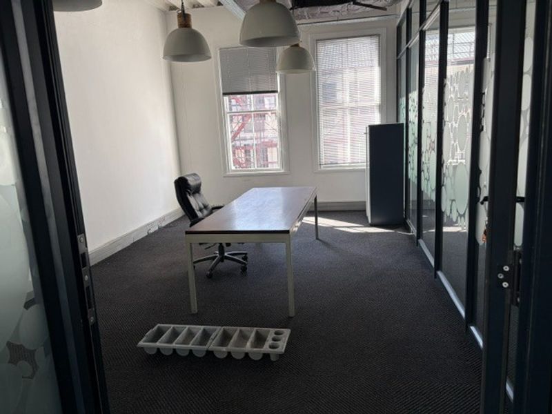 A professional office space featuring glass partition walls, carpeted flooring, and large windows providing natural light, with exposed ceiling ducting for a modern industrial aesthetic.