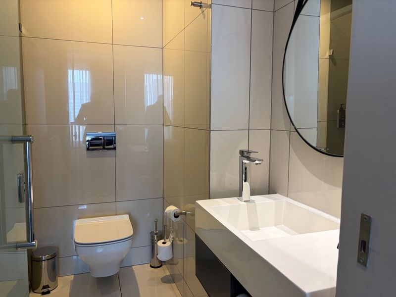 Modern bathroom featuring a wall-mounted toilet, sleek vanity basin with chrome mixer tap, and floor-to-ceiling wall tiling.