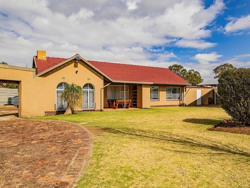 Rear view of a single-story house featuring a red tiled roof, arched windows, a covered patio, and a spacious garden with a brick paved driveway.