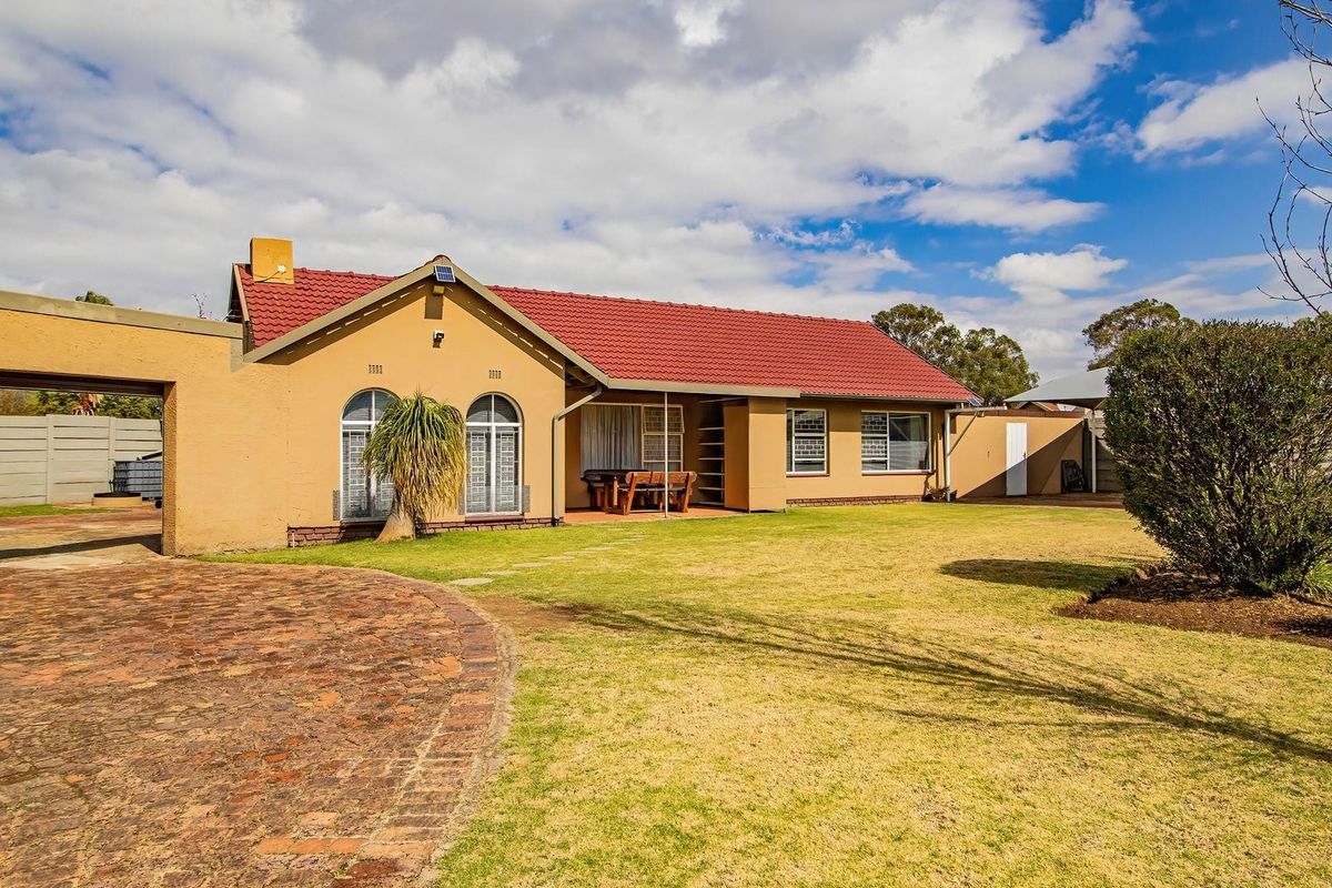 Rear view of a single-story house featuring a red tiled roof, arched windows, a covered patio, and a spacious garden with a brick paved driveway.