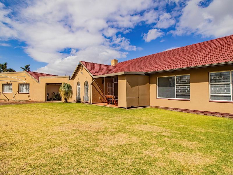 Rear view of the house featuring a tiled roof, brick facade, covered patio area, and a spacious lawn with an attached garage.