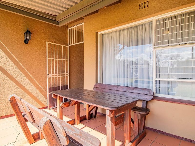 A covered patio area featuring tiled flooring, security gates, and protective window bars, providing a functional outdoor space.