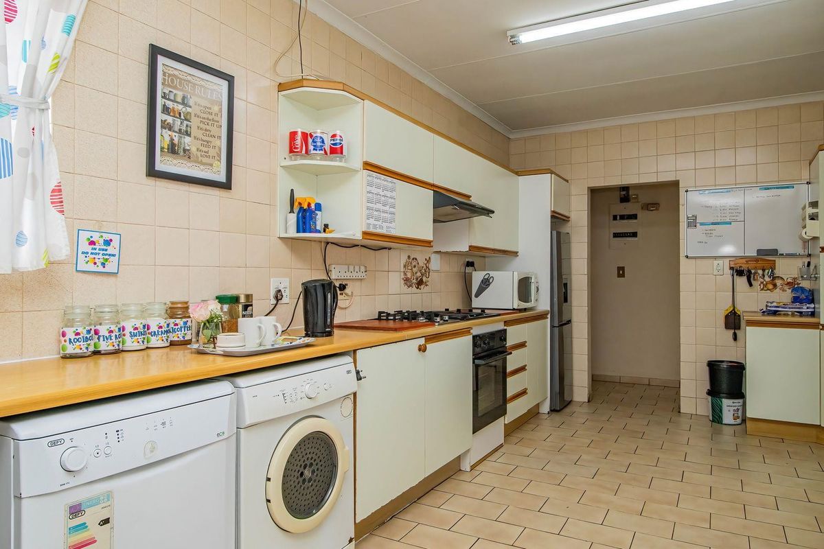 Functional kitchen featuring built-in cabinetry, gas hob, oven, extractor fan, and tiled finishes, offering a practical layout with integrated laundry appliance space.