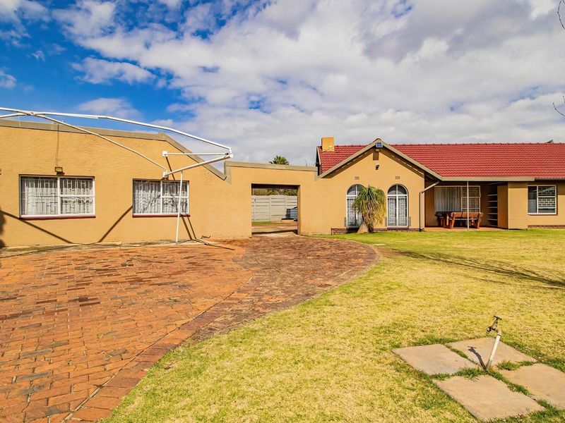 Rear view of the house featuring a brick paved driveway, a spacious lawn, and a covered patio area with a tiled roof.