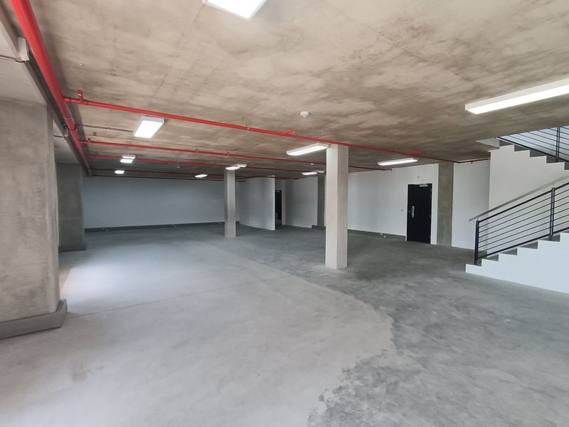 A spacious, open-plan industrial utility area featuring exposed concrete ceilings, fire sprinkler systems, and a staircase with metal railings.