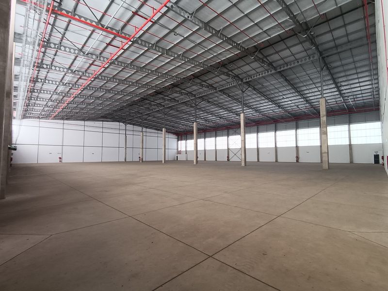 Spacious industrial warehouse featuring high ceilings, exposed steel truss roofing, fire sprinkler system, and durable concrete flooring, suitable for various commercial or storage operations.