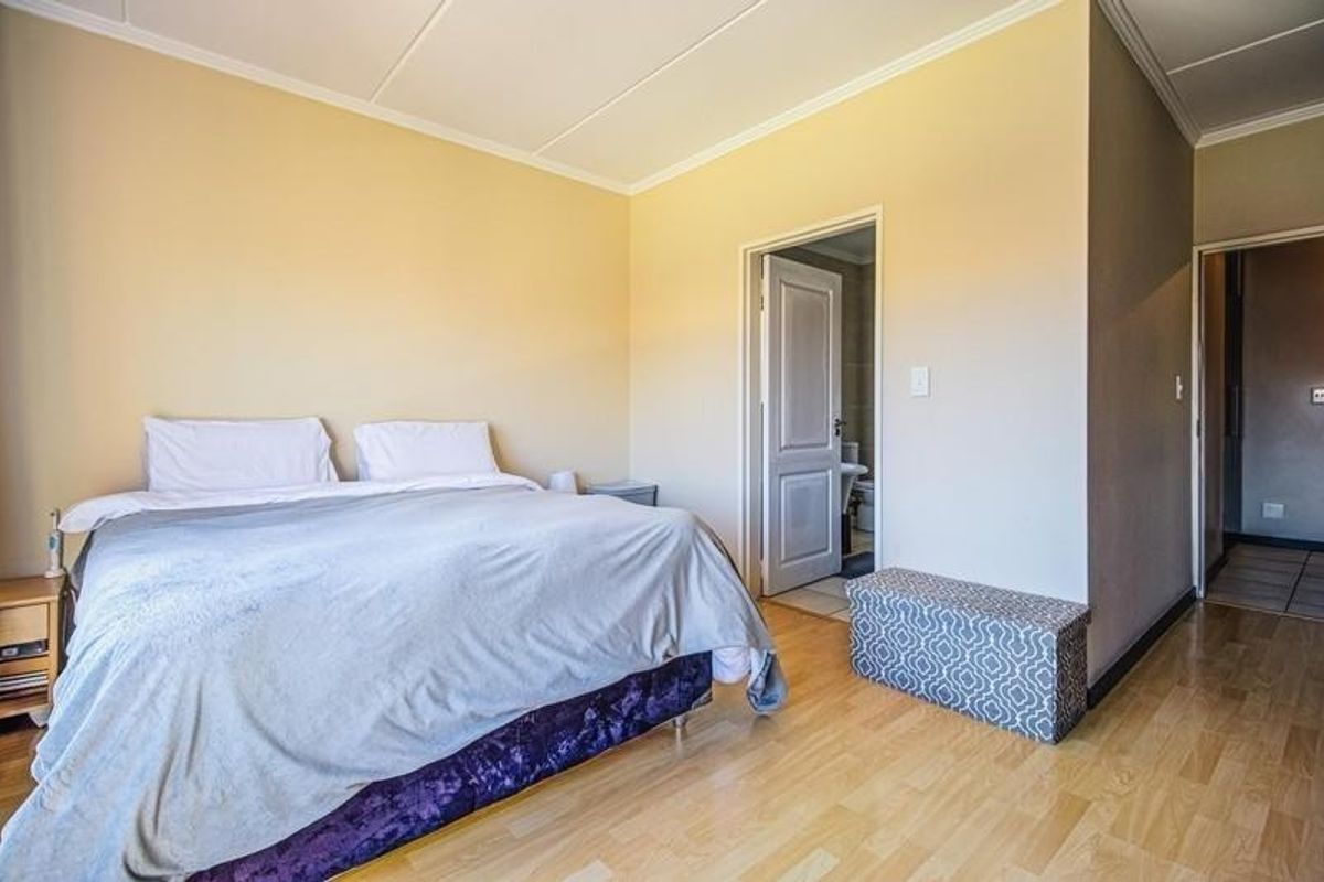 A spacious bedroom featuring light-toned laminate flooring, neutral wall finishes, and direct access to an en-suite bathroom.