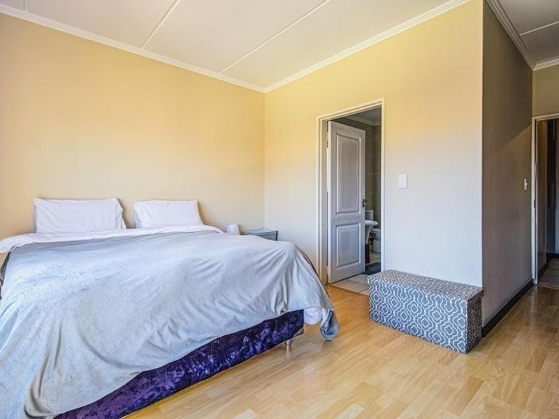 A spacious bedroom featuring light-toned laminate flooring, neutral wall finishes, and direct access to an en-suite bathroom.