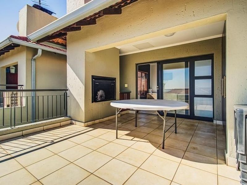 A covered patio area featuring tiled flooring, a built-in braai, and sliding glass doors providing access to the interior living space.