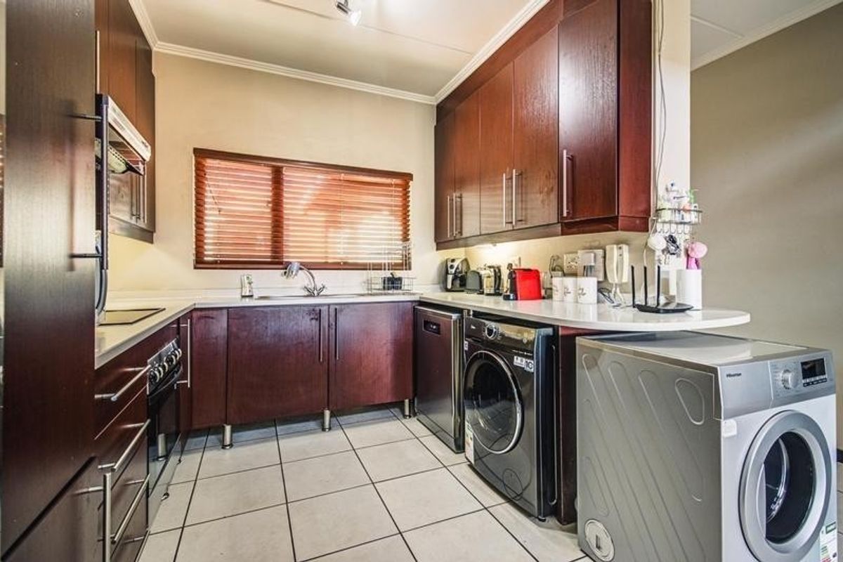A functional kitchen featuring dark wood cabinetry, tiled flooring, integrated appliances, and ample counter space with a window providing natural light.