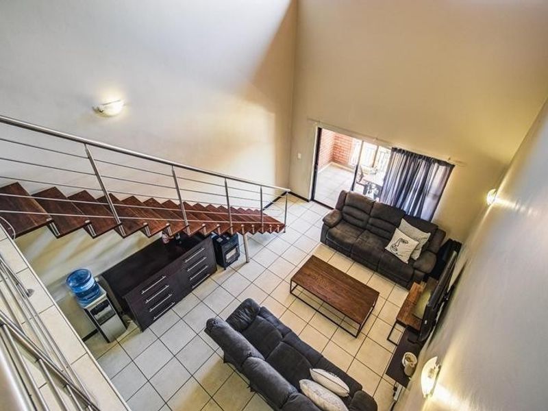 Spacious double-volume living area featuring a modern staircase with stainless steel balustrades, tiled flooring, and direct access to an outdoor patio.