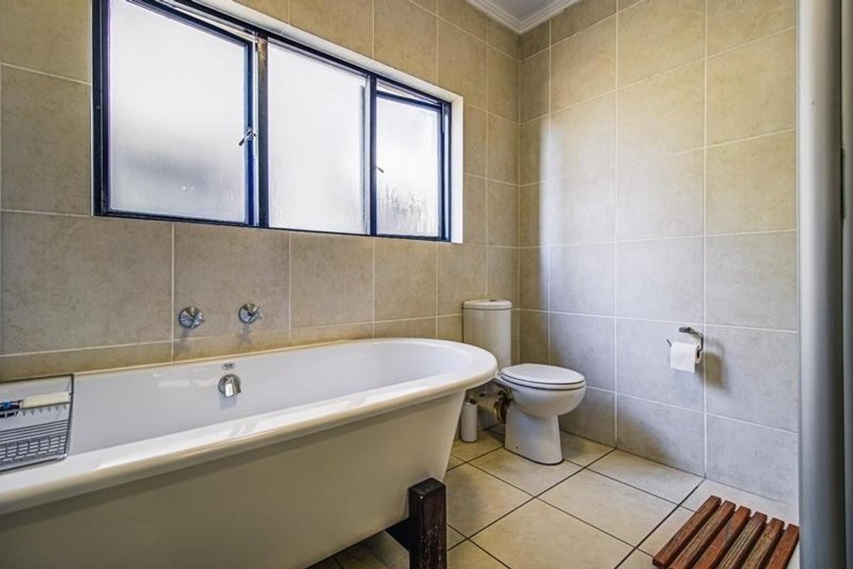 A functional bathroom featuring a classic freestanding bathtub, a standard toilet, and neutral wall and floor tiling with natural light from a frosted window.