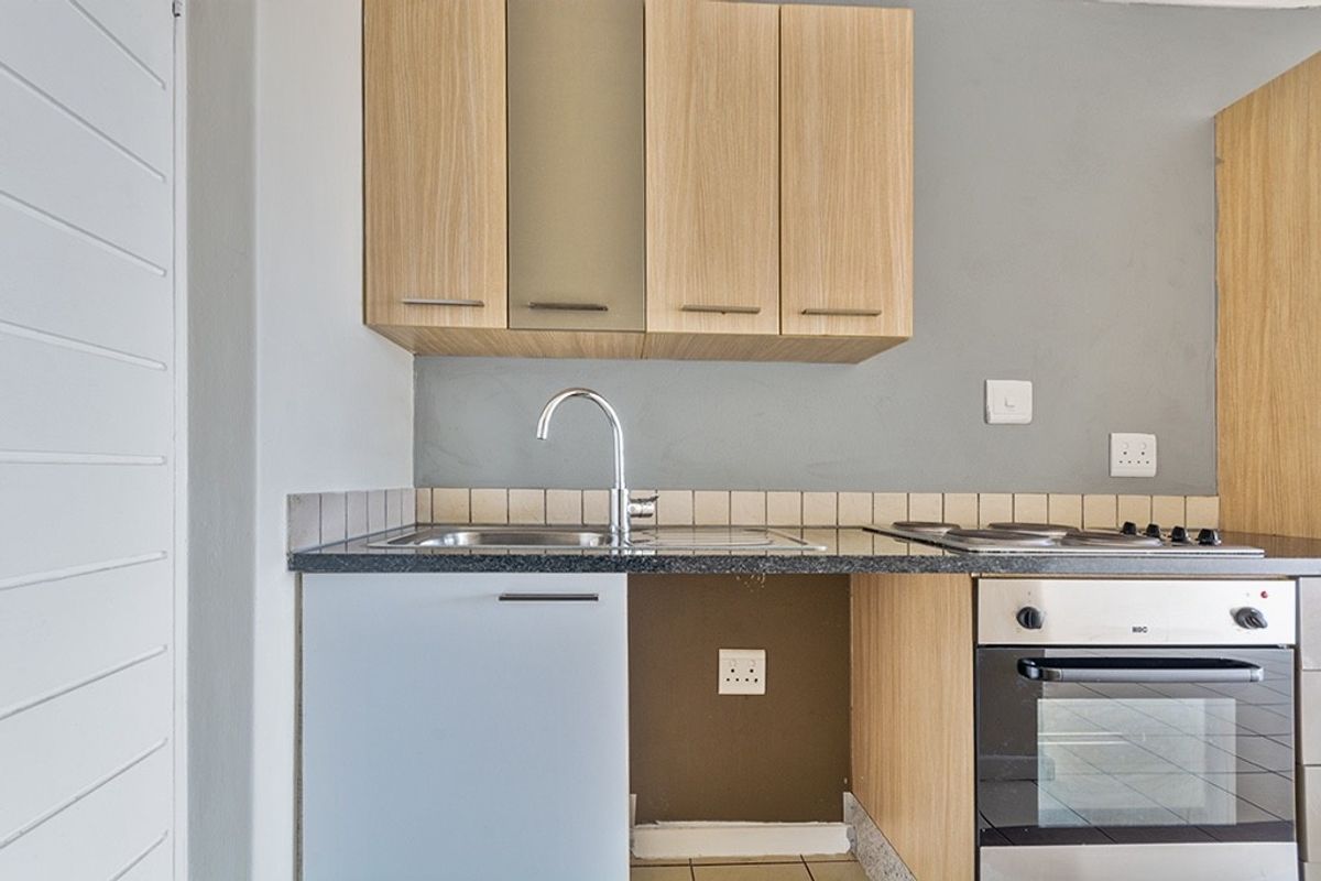 Compact kitchen featuring light wood cabinetry, granite countertops, a stainless steel sink, and a built-in oven with an electric hob.