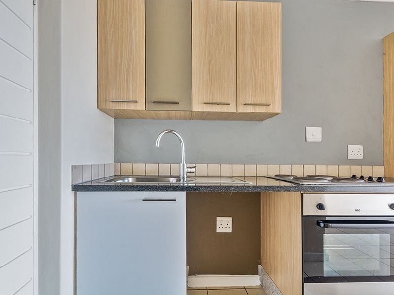 Compact kitchen featuring light wood cabinetry, granite countertops, a stainless steel sink, and a built-in oven with an electric hob.