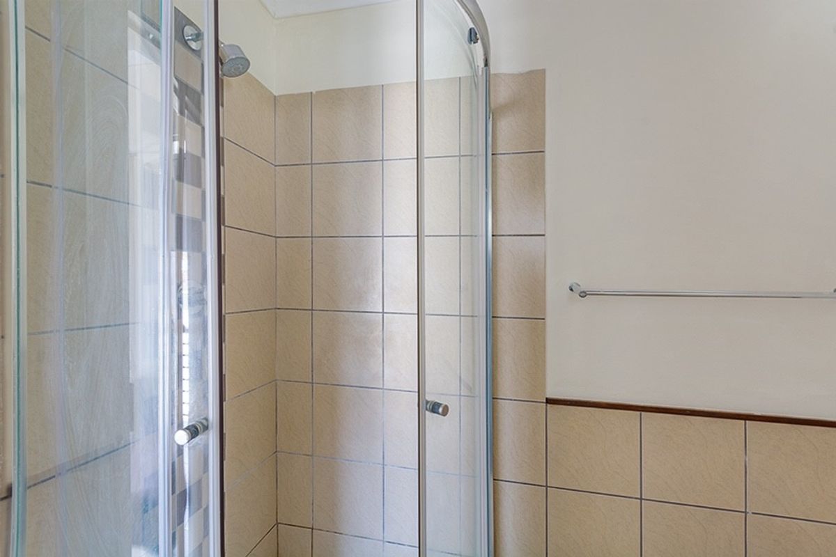 A functional bathroom shower area featuring a curved glass enclosure, neutral wall tiling, and a fitted towel rail.