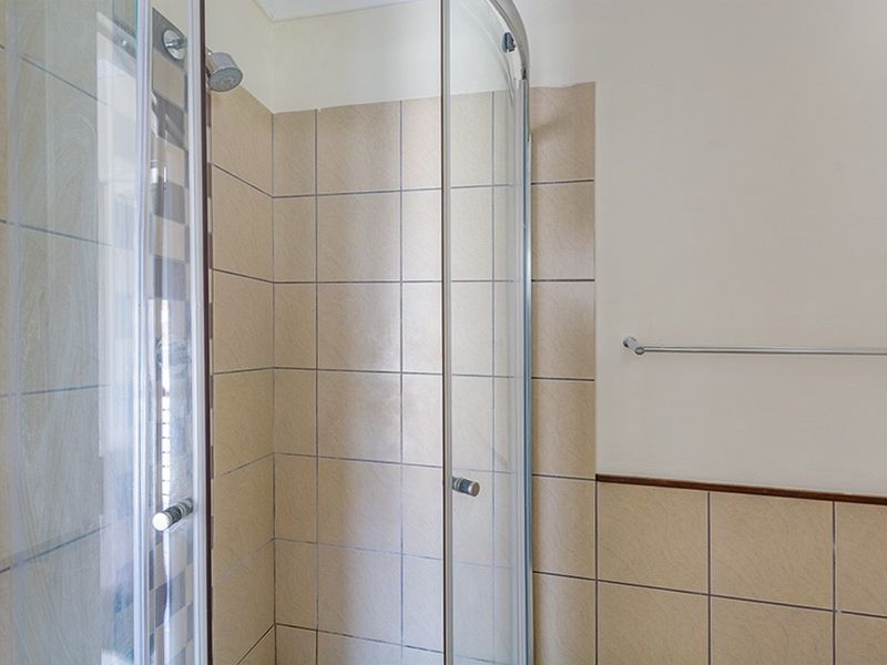 A functional bathroom shower area featuring a curved glass enclosure, neutral wall tiling, and a fitted towel rail.