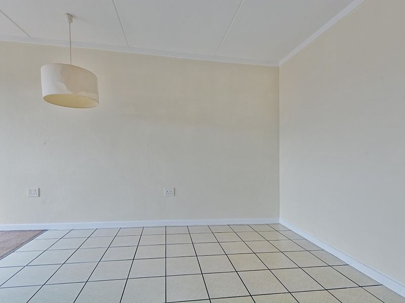 An empty, neutral-toned living area featuring tiled flooring, a simple pendant light fixture, and clean wall finishes, ready for personalization.