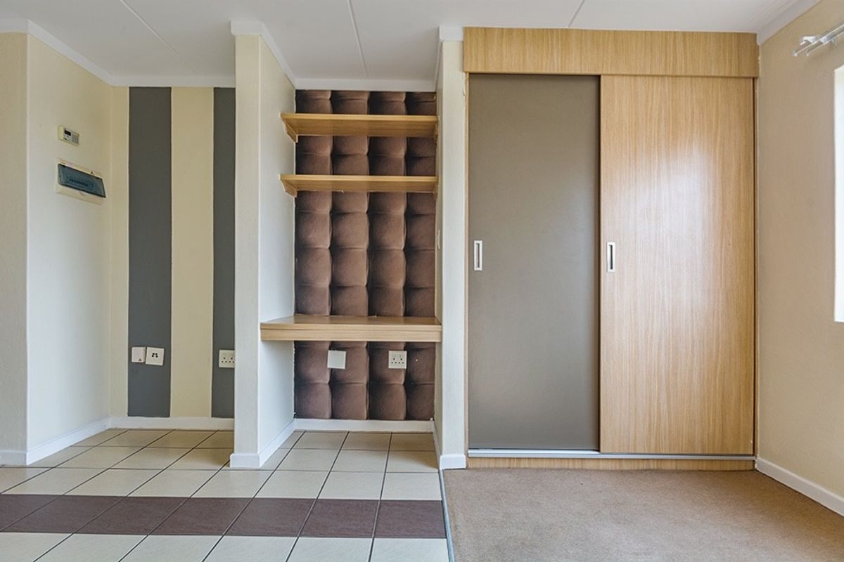 A bedroom featuring a built-in wardrobe with sliding doors, a dedicated built-in desk area with floating shelves, and a mix of tiled and carpeted flooring.