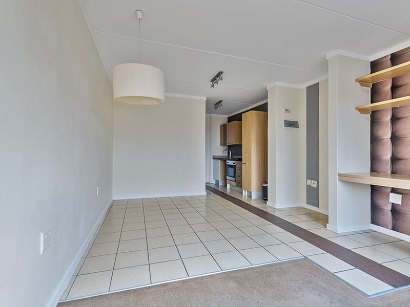Open-plan living and kitchen area featuring tiled flooring, built-in cabinetry, integrated appliances, and floating shelving, offering a versatile and functional layout.