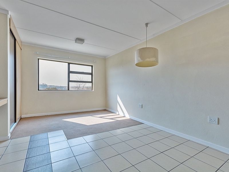 An empty living area featuring a mix of tiled and carpeted flooring, a built-in cupboard, and a large window providing natural light.