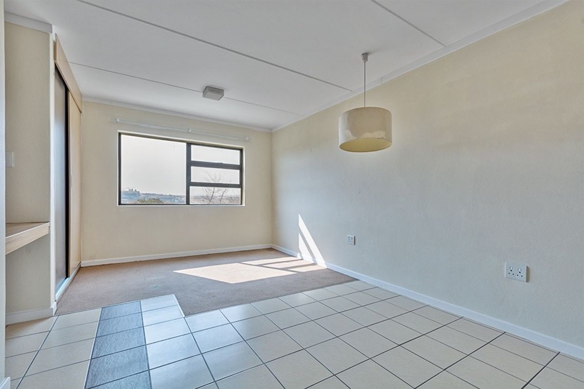 An empty living area featuring a mix of tiled and carpeted flooring, a built-in cupboard, and a large window providing natural light.