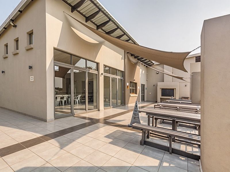 Spacious outdoor patio area featuring tiled flooring, a built-in braai, and overhead shade sails, providing a functional space for outdoor entertainment.