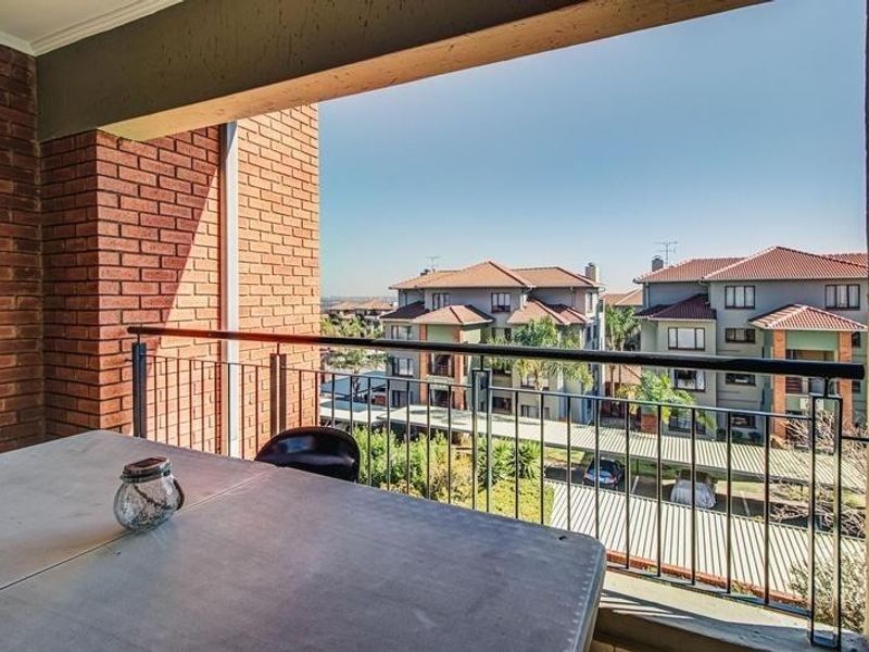 A covered balcony featuring exposed brick walls and a metal railing, offering an elevated view of the surrounding residential complex.