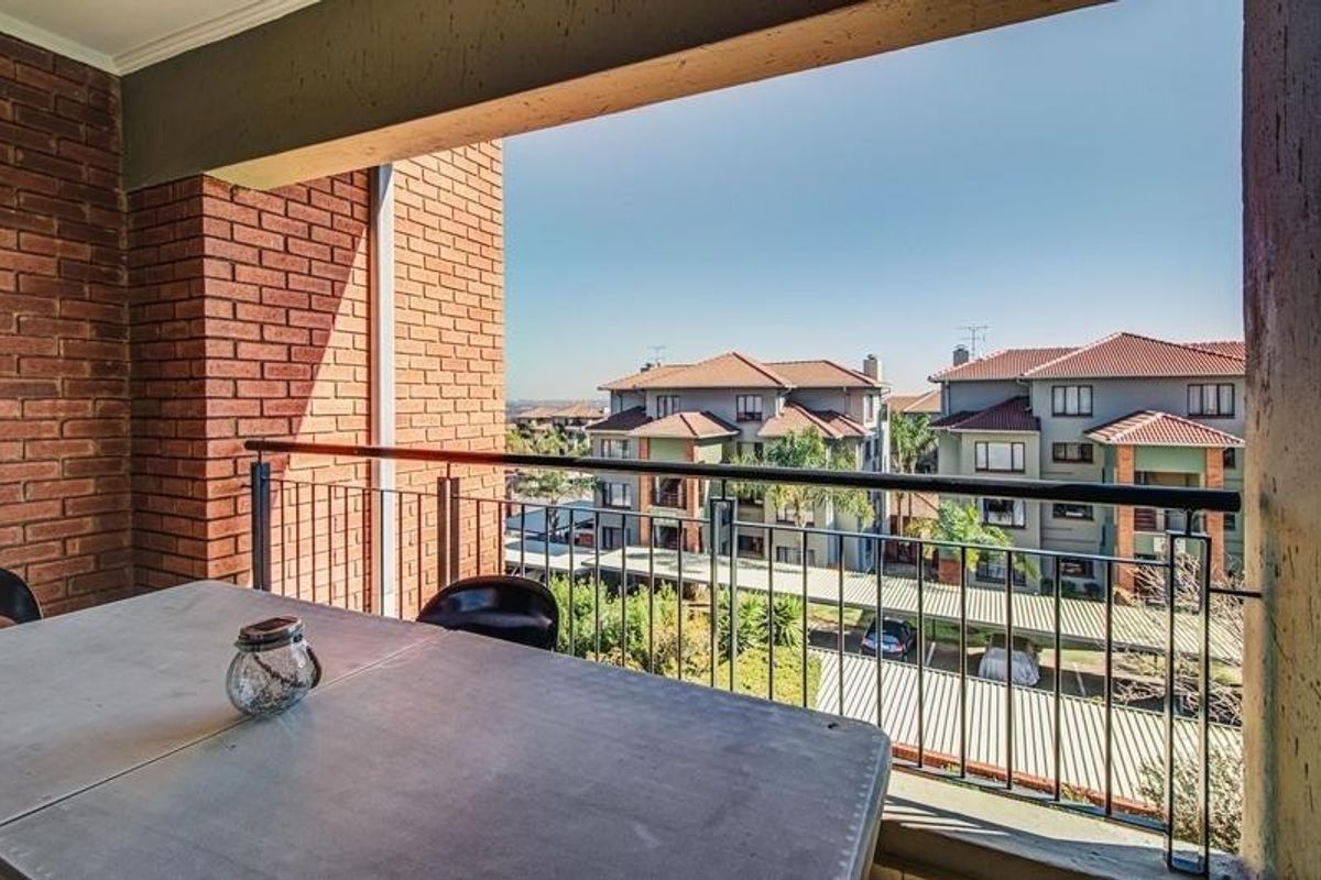 A covered balcony featuring exposed brick walls and a metal railing, offering an elevated view of the surrounding residential complex.
