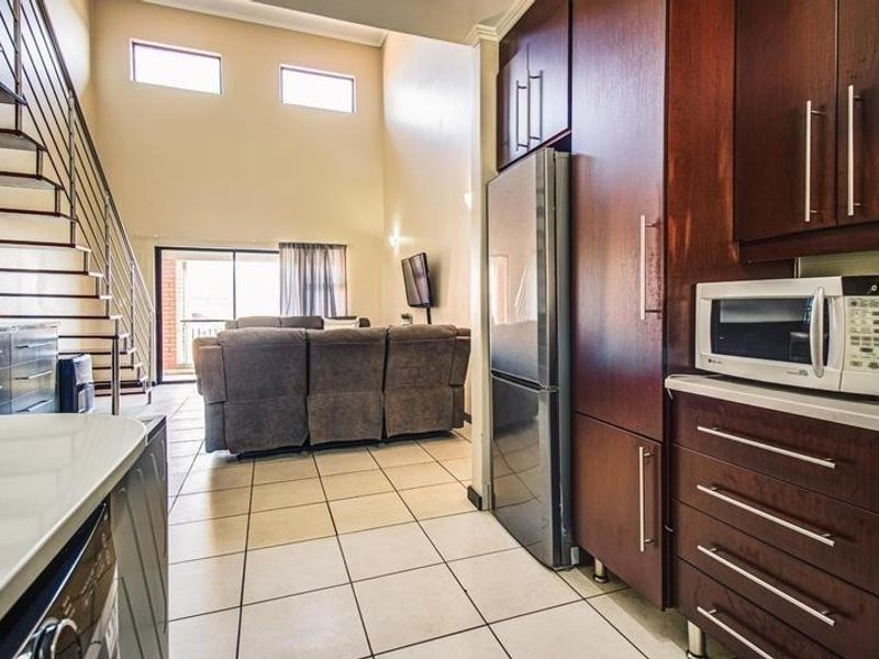 Open-plan living area featuring a kitchen with dark wood cabinetry, high ceilings, and a staircase leading to an upper level.