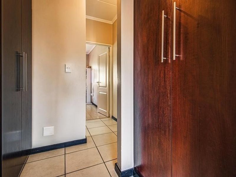 A clean, well-maintained hallway featuring built-in cupboards with dark wood finishes and neutral tiled flooring, leading to an adjacent room.