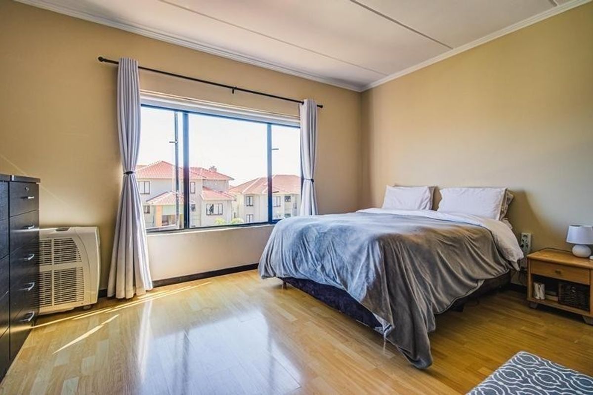 A well-lit bedroom featuring laminate flooring, a large window with curtain rods, and neutral wall finishes, offering a comfortable and functional living space.
