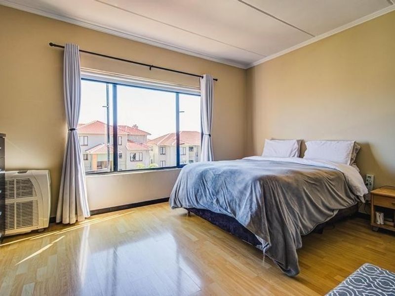 A well-lit bedroom featuring laminate flooring, a large window with curtain rods, and neutral wall finishes, offering a comfortable and functional living space.