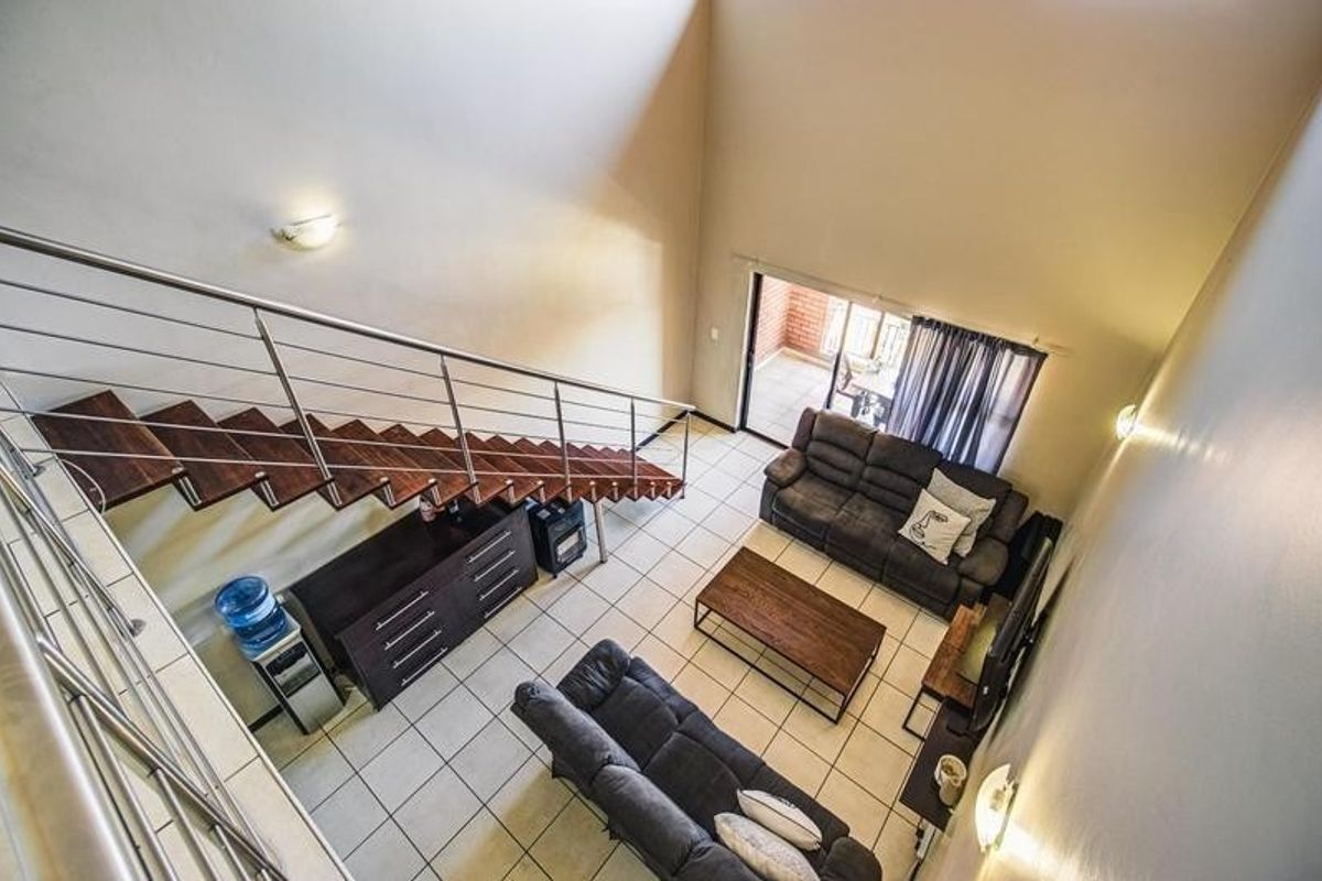 Spacious double-volume living area featuring a modern staircase with stainless steel balustrades, tiled flooring, and direct access to an outdoor patio.
