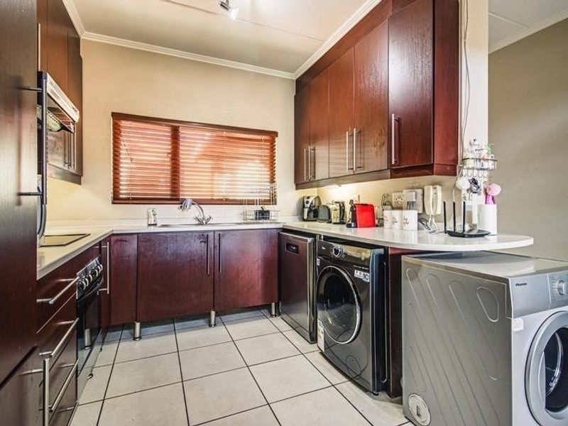 Functional scullery featuring dark wood cabinetry, laminate countertops, tiled flooring, and integrated laundry appliance connections.