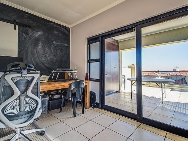 Home office space featuring tiled flooring, a chalkboard wall, and large sliding glass doors providing direct access to an outdoor balcony area.