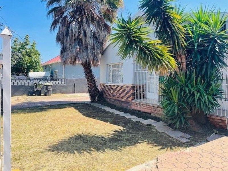 Front exterior view of the house featuring a paved driveway, security gates, and established garden area.