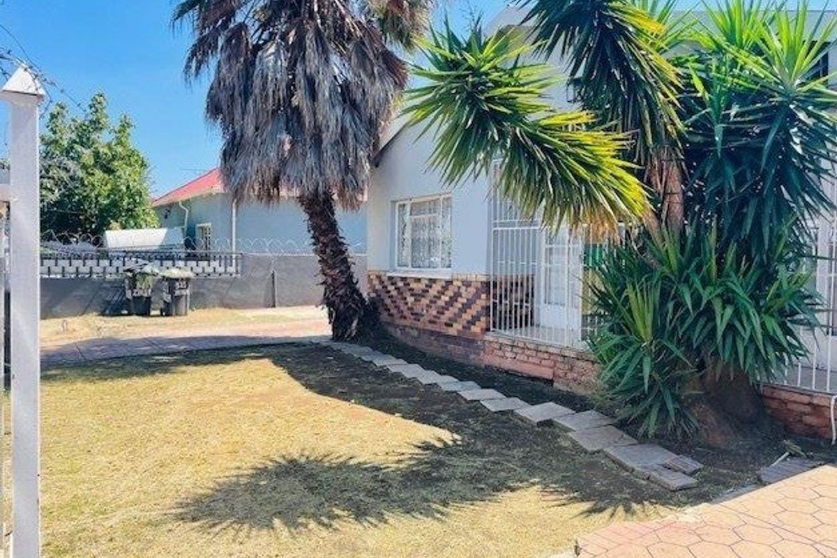 Front exterior view of the house featuring a paved driveway, security gates, and established garden area.