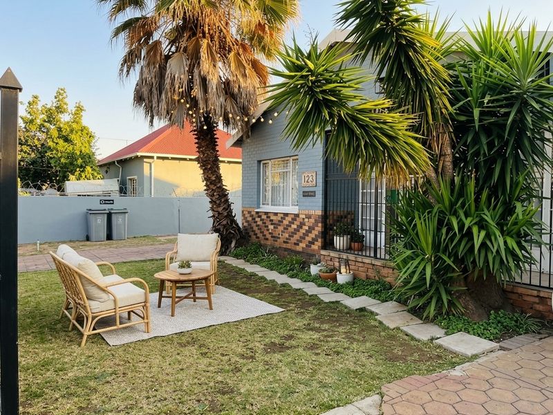 Front garden area featuring a brick facade, security gate, and paved walkway, with established palm trees and perimeter walling.