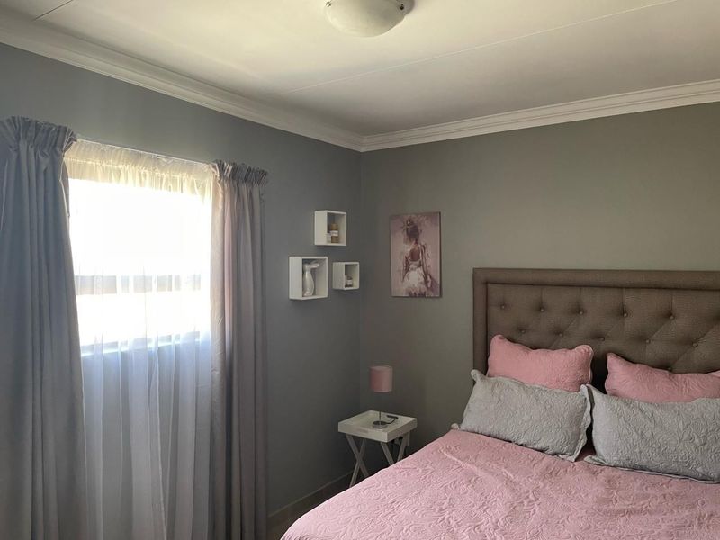 A well-maintained bedroom featuring neutral grey walls, crown molding, and a window with natural light.