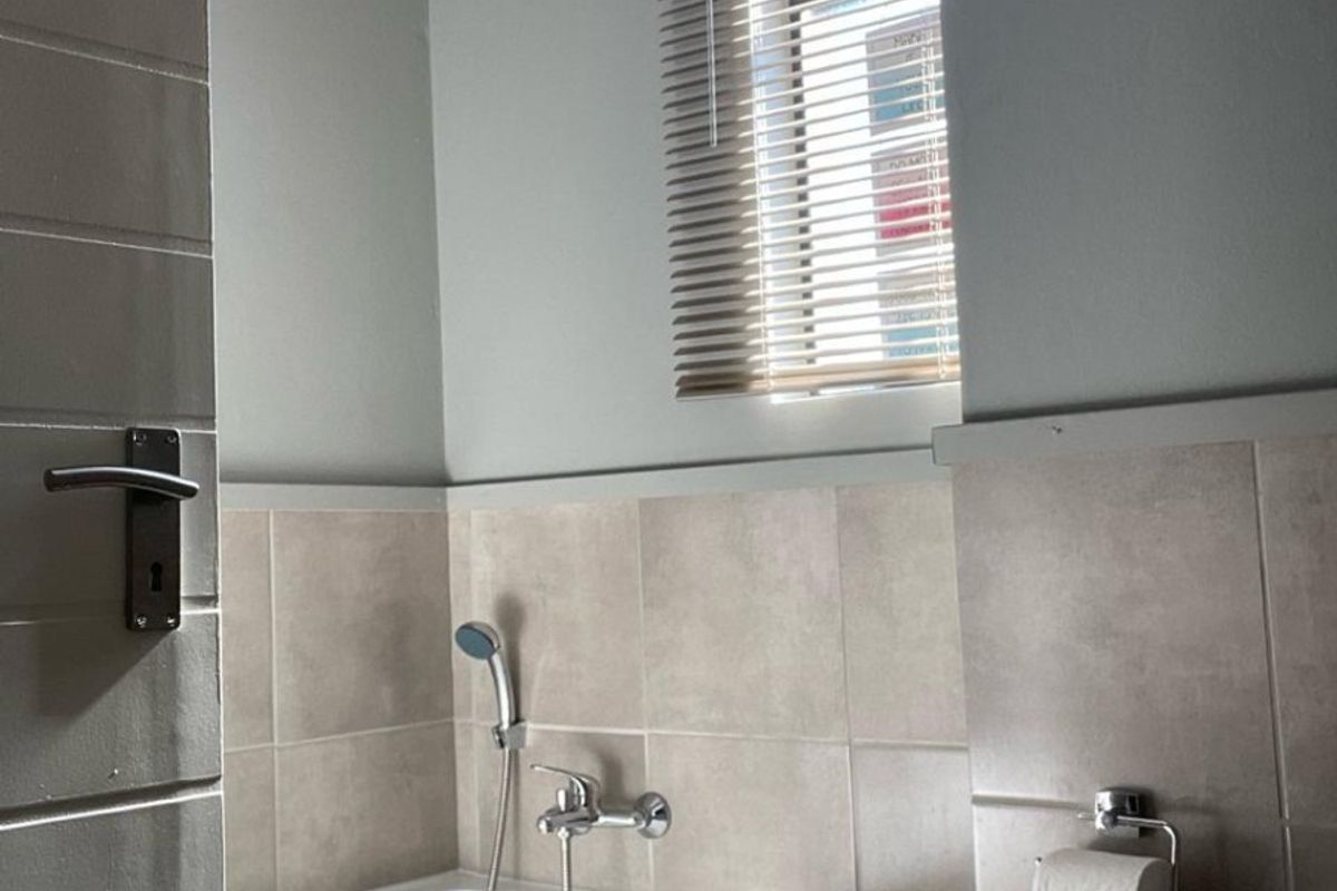 A clean, neutral-toned bathroom featuring a built-in bathtub with a handheld shower mixer and tiled wall finishes.