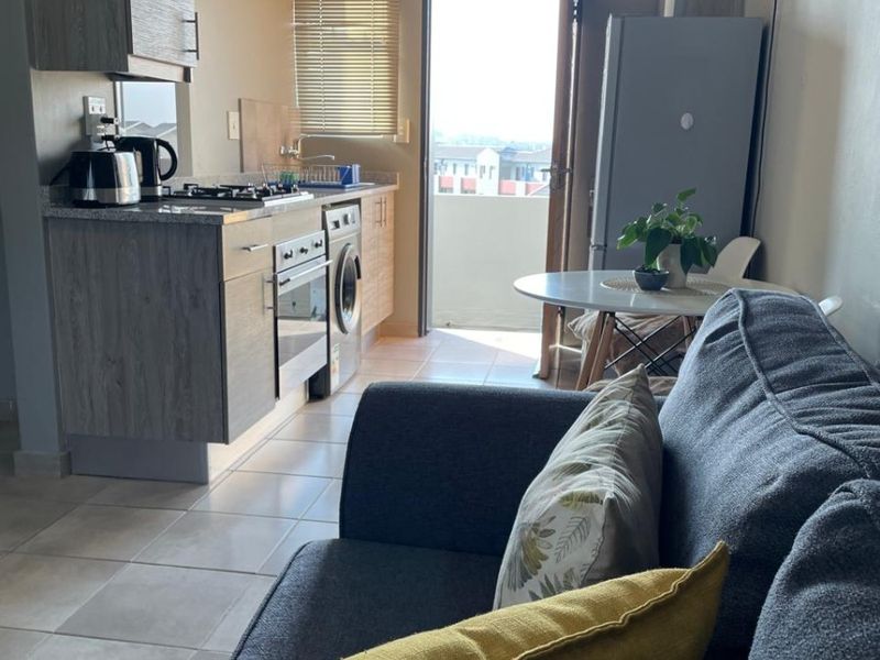 Open-plan living area featuring a compact kitchen with modern cabinetry, granite countertops, and integrated appliances, leading directly to an outdoor balcony.