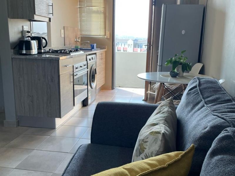 Open-plan living area featuring a compact kitchen with modern cabinetry, granite countertops, and integrated appliances, leading directly to an outdoor balcony.
