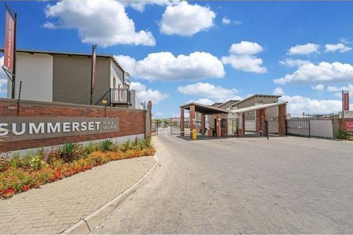 The entrance to Summerset Place Village featuring a secure gated access point, brick boundary wall, and paved driveway.