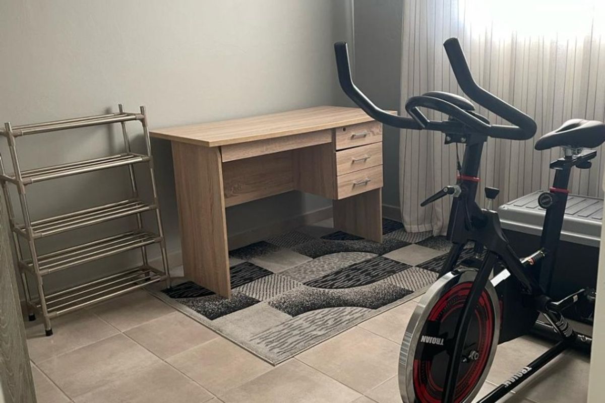 A functional bedroom space featuring neutral tiled flooring and natural light, currently utilized as a home office and fitness area.
