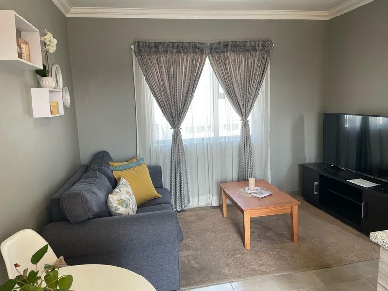 A cozy living room featuring neutral grey walls, crown molding, and tiled flooring, providing a comfortable and well-maintained space.