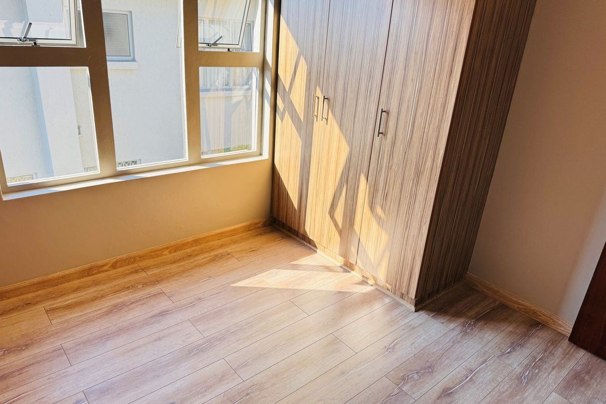 A bright, empty bedroom featuring modern wood-look laminate flooring and a built-in wardrobe with wood-grain finish.