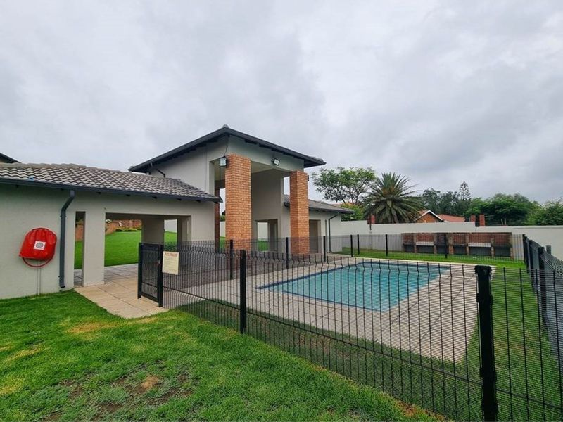 Communal pool area featuring a paved deck, brick pillars, and built-in braai facilities within a secure fenced enclosure.
