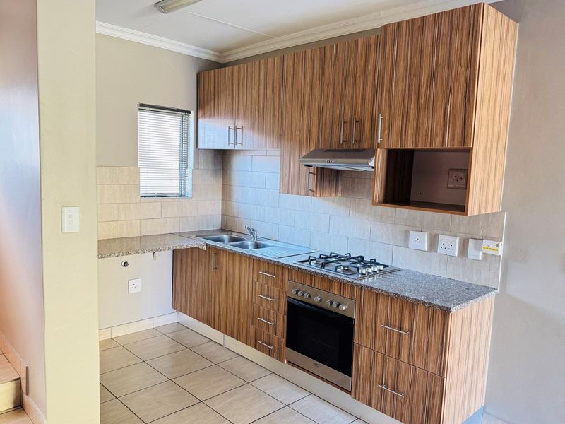 A functional kitchen featuring wood-look laminate cabinetry, granite countertops, a built-in oven with gas hob, and tiled flooring.